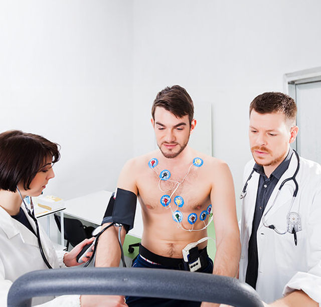 Dois médicos analisam um ECG de esforço num homem, que utiliza elétrodos e equipamentos como passadeira ou bicicleta ergométrica para o exame.
