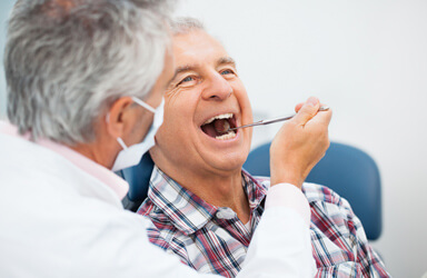 Homem na consulta de dentista, sentado na cadeira do consultório com um ar feliz, com o dentista a examinar os seus dentes.