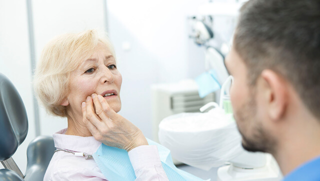 Paciente no consultório de dentista, com a mão na cara a descrever as suas dores de dentes.