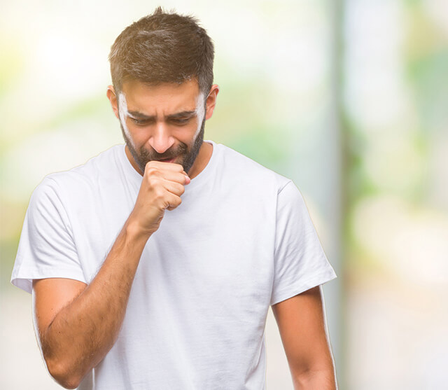 Homem ao ar livre, que sofre de rinite alérgica, a cobrir a boca com a mão enquanto tosse, um dos sintomas da rinite alérgica.