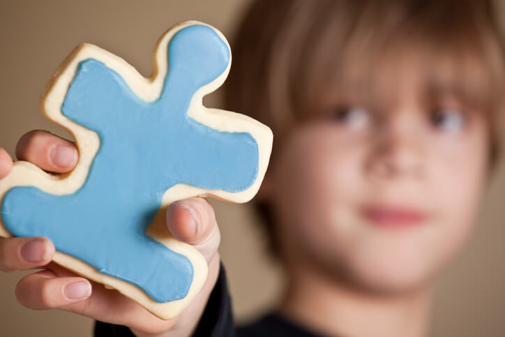Criança que sofre de síndrome de asperger a segurar numa bolacha em forma de pessoa.