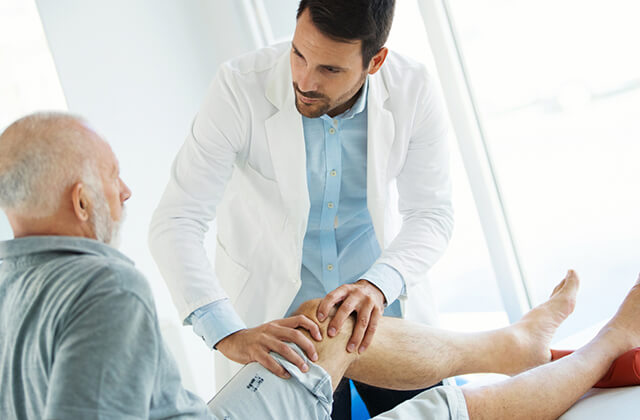 Médico a examinar o joelho de um paciente idoso no consultório, ilustrando a avaliação e cuidado no tratamento de problemas reumatológicos, como a artrose.
