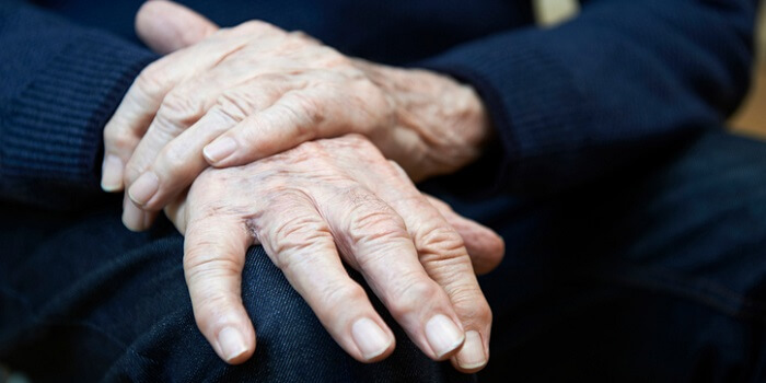 As mãos de uma pessoa idosa, pousadas no joelho, que representam a certeza da efemeridade da vida e a fragilidade humana, causadas também pelo Parkinson.