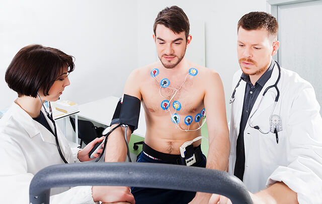 Dois médicos analisam um ECG de esforço num homem, que utiliza elétrodos e equipamentos como passadeira ou bicicleta ergométrica para o exame.
