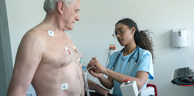 Uma médica a colocar elétrodos no peito de um homem idoso para realizar um exame cardíaco.