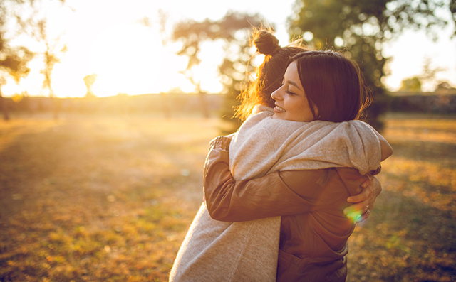 Duas mulheres abraçadas ao ar livre, símbolo da importância da socialização para a nossa saúde mental.