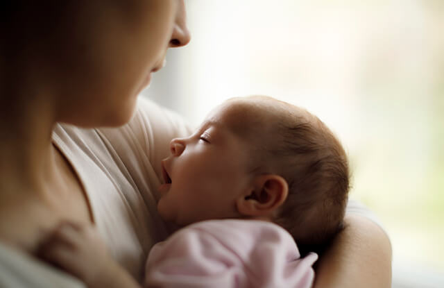 Mulher, que atravessa a complexidade de mudanças físicas, emocionais e comportamentais que podem ocorrer no pós-parto, com o seu bebé ao colo.