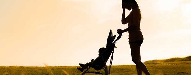 Uma mulher ao ar livre a passear o seu filho num carrinho de bebé. Um exercício para controlar as grandes mudanças provenientes do pós-parto.