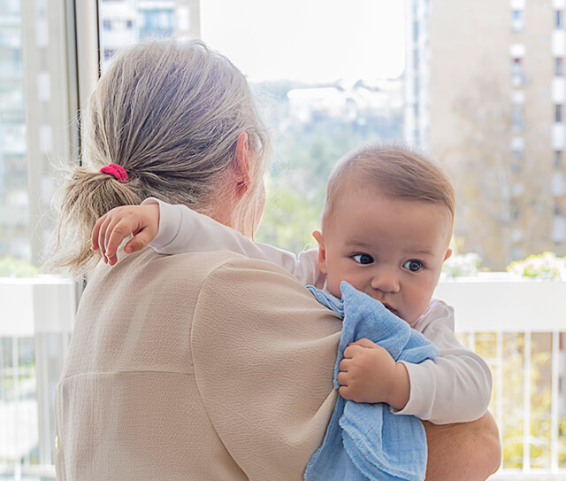 Mulher, dentro de casa, com o seu bebé ao colo. Pronta para enfrentar esta fase do pós-parto onde existem riscos de depressão.