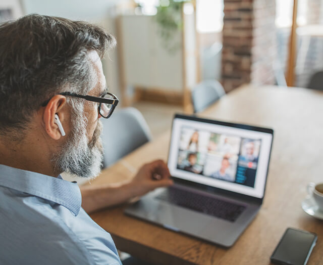 Homem sentado à secretária enquanto está numa call de trabalho. Sinal de que nos dias de hoje passamos muito tempo sentados.