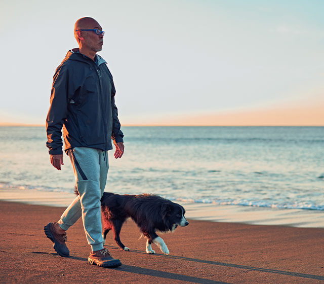 Homem à beira-mar a caminhar o seu cão, ao fim o dia.