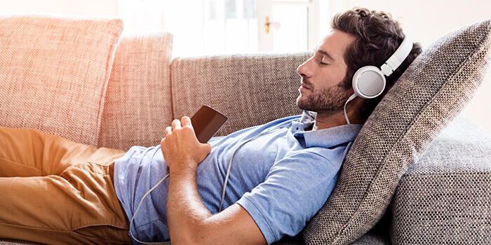 Homem com ar relaxado deitado no sofá, a ouvir música.
