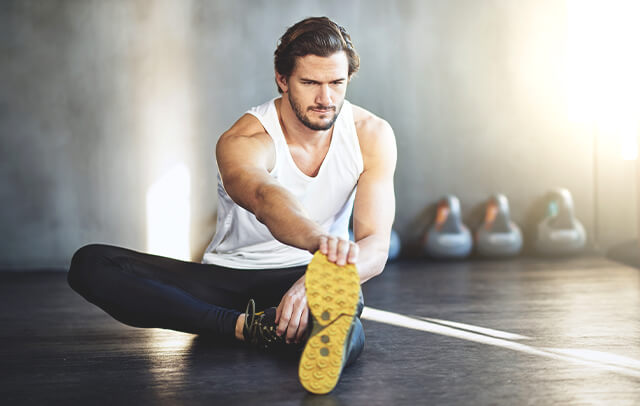 Homem, no ginásio, a alongar antes de iniciar o treino prevenindo eventuais lesões.