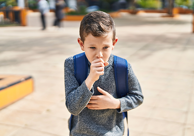 Rapaz com mochila às costas a tossir para a mão